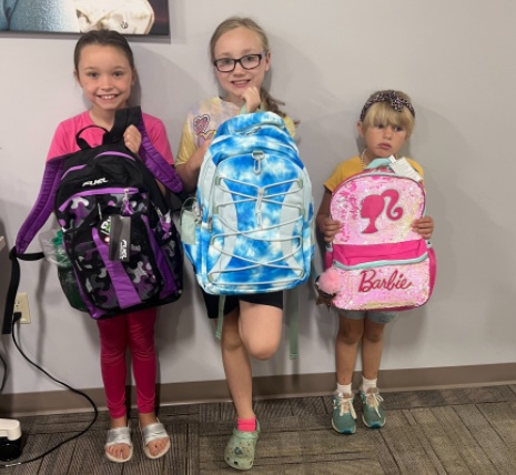Three children standing outside a Penquis office proudly displaying their new backpacks and lunchboxes received through the We've Got Your Back (WGYB) backpack drive.